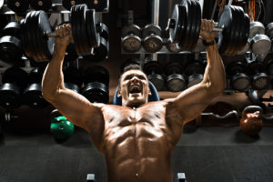 very power athletic guy bodybuilder ,  execute exercise press of dumbbells on pectoral muscle, in gym